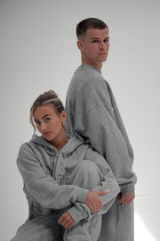 Two models in matching grey marl hoodie and jogger sets, one seated in front of the other